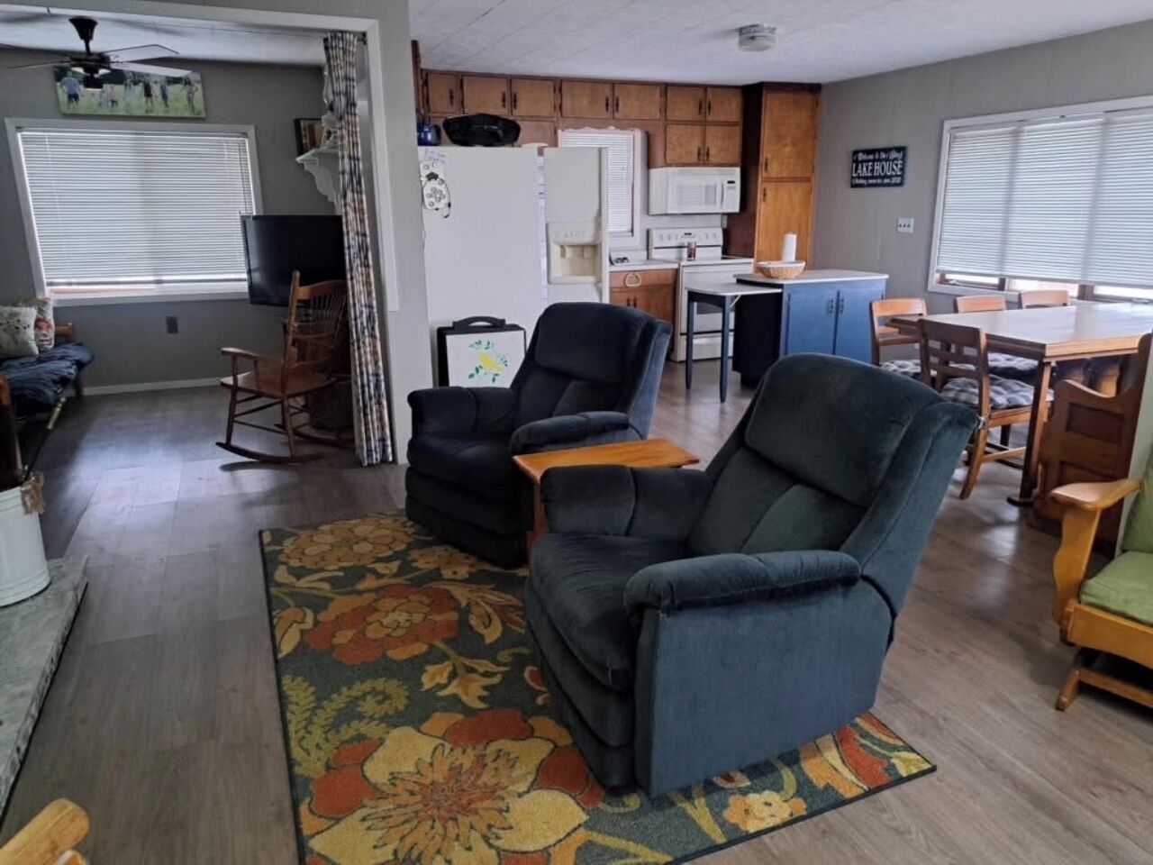 A living room with a sofa, chairs, a coffee table, a TV, and a kitchen area with cabinets and appliances.