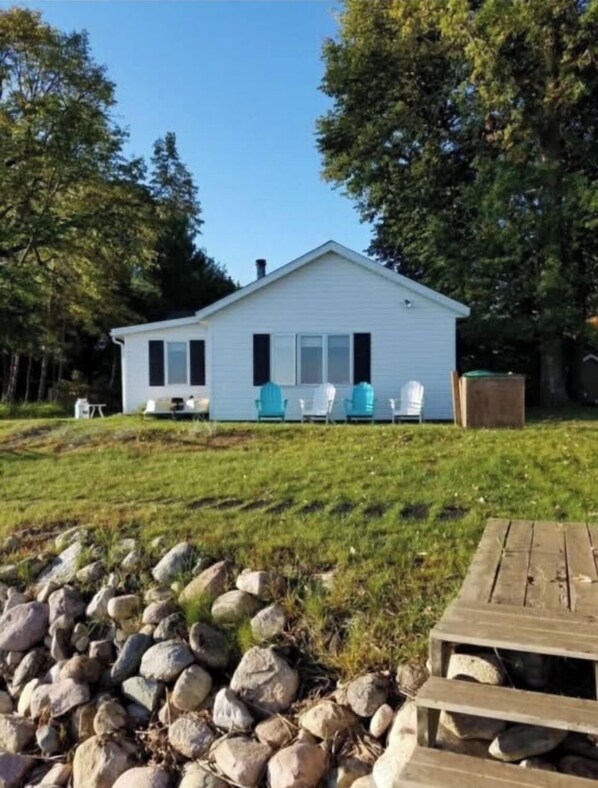 A single-story house with a front porch, a small deck, and a stone wall in the foreground.