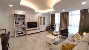 Un salon moderne doté d’un téléviseur à écran plat, de meubles blancs, d’une table basse et d’un canapé agrémenté de coussins.