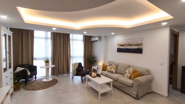 Un salon moderne avec un canapé, une table basse et un téléviseur. On y trouve également une table à manger avec des chaises, une plante et une fenêtre avec des rideaux.