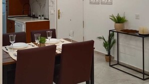 Un espace de salle à manger moderne avec une table dressée pour quatre personnes, une cuisine en arrière-plan et des œuvres d'art décoratives au mur.