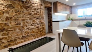 Una cocina moderna con pared de piedra, armarios blancos y una zona de comedor con sillas.