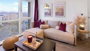 Ein modernes Wohnzimmer mit einer Couch, einem Couchtisch, einer Lampe und Blick auf die Stadt durch große Fenster.