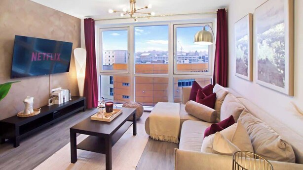 Ein modernes Wohnzimmer mit großem Fenster, Flachbildfernseher, einer Couch, einem Couchtisch und Kunstwerken an den Wänden.