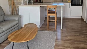 A modern kitchen with a stone accent wall, a dining area with a wooden table and chair, and a grey sofa in a living space.