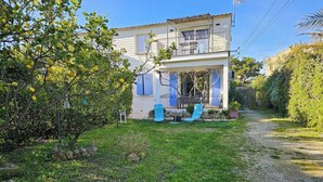 A two-story house with a balcony, a gravel path, and a garden with a tree bearing yellow fruit. - - (Hyères)
