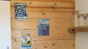 A kitchen with wooden walls, a hanging light bulb, and various decorative items including a sailboat poster, a beach-themed sign, and flamingos. - - (Hyères)