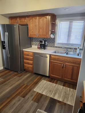 A modern kitchen with wooden cabinets, stainless steel appliances, a coffee maker, and a window with blinds.