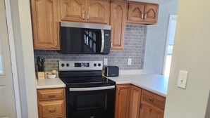 A compact kitchen with wooden cabinets, a stainless steel stove, a microwave, and a toaster. - Spacious 4-bedroom house in Cherokee with AC (Cherokee)
