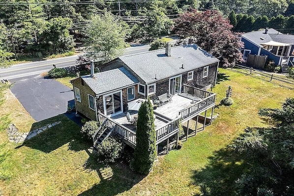 A two-story house with a deck, a garage, and a large tree in front.