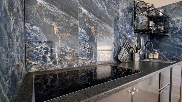 A kitchen with a black granite countertop, a marble backsplash, and a black pot rack. - Convenient 3BR Apartment near ExCel, O2 Arena w/Parking, Link to Central London (London)