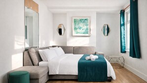 A modern bedroom with a grey sofa bed, a small round ottoman, and a teal throw blanket. - Convenient 3BR Apartment near ExCel, O2 Arena w/Parking, Link to Central London (London)