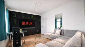 A modern living room with a grey sofa, a glass coffee table, and a flat-screen TV mounted on a black wall. - Convenient 3BR Apartment near ExCel, O2 Arena w/Parking, Link to Central London (London)