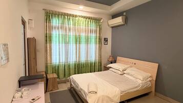 A neatly arranged hotel room with a bed, a desk, a chair, a ceiling fan, and an air conditioning unit.