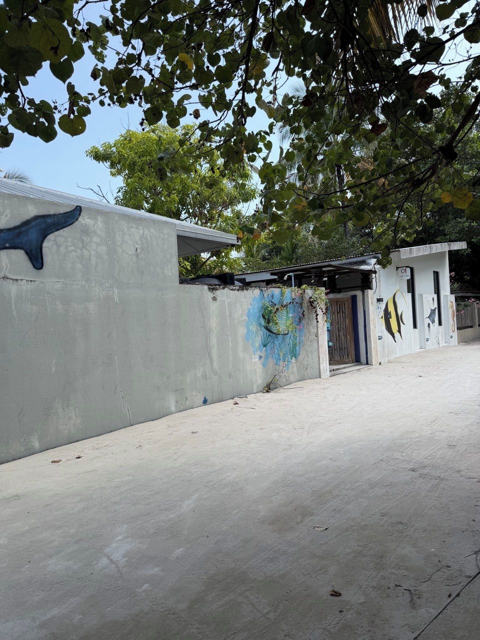 A concrete building with a mural, a door, and a small structure with a roof.