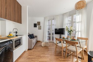 Eine moderne Küche mit Waschmaschine, ein Essbereich mit Tisch und Stühlen sowie ein Fernseher im Hintergrund.