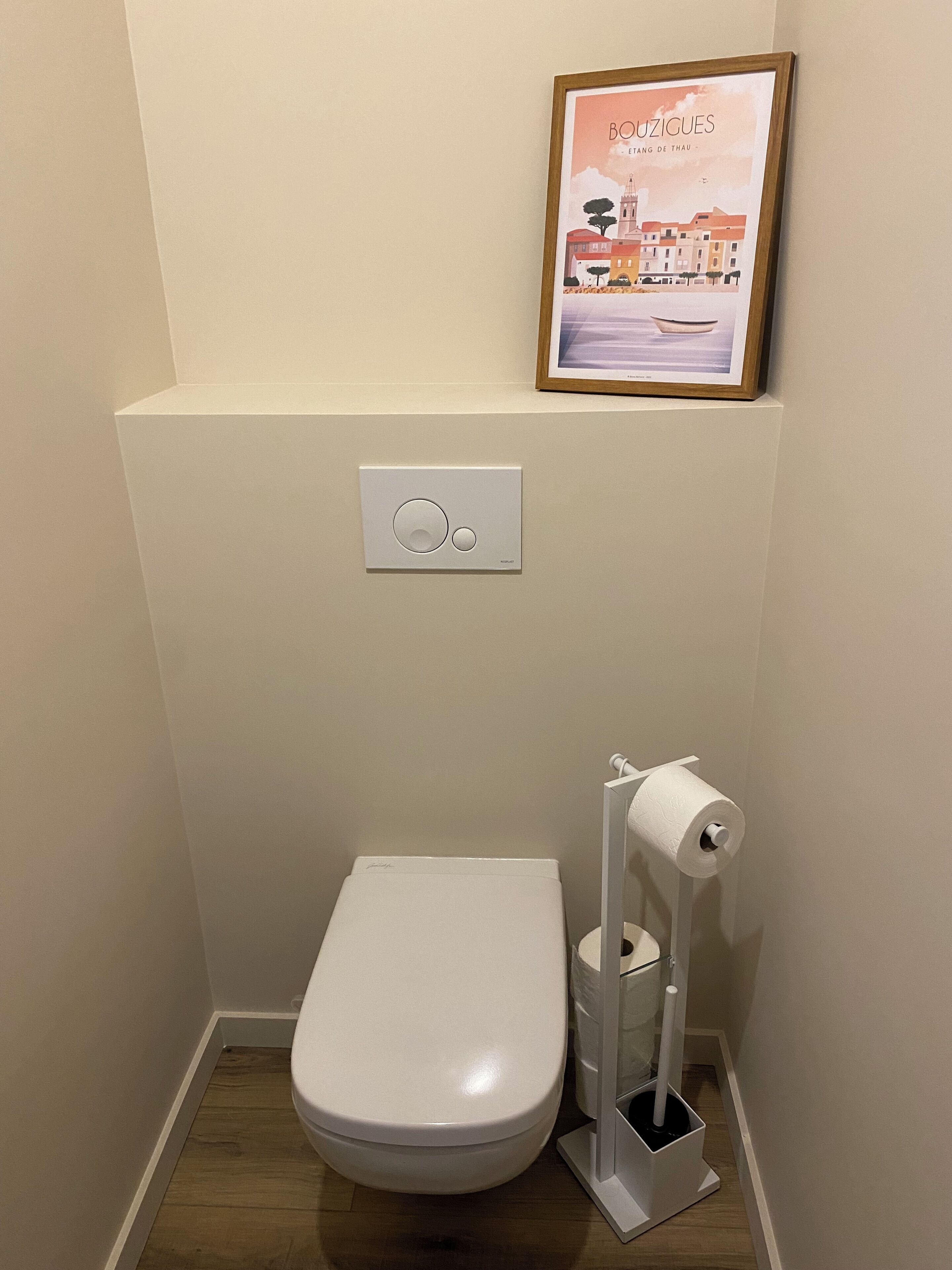 Une petite salle de bain moderne équipée de toilettes, d’un porte-rouleau de papier toilette et d’un système de chasse d’eau mural.