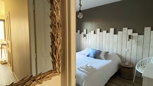 A bedroom with a bed, a white chair, a mirror, and a hanging light fixture. - The balconies of Bouzigues l'hippocampe (Bouzigues)