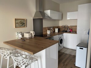 Cocina compacta con encimera de madera, lavadora, horno empotrado y refrigerador pequeño.