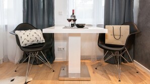 A modern room with a white table, two black chairs with fur cushions, a wine bottle, and a shopping bag. - Exclusive studio business apartment (Neu-Isenburg)