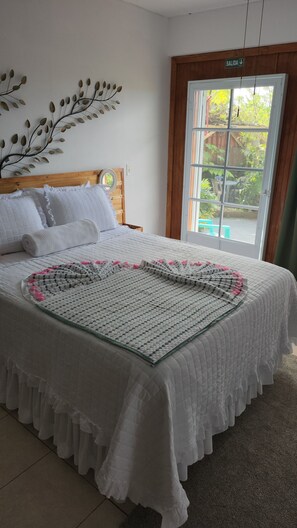 Un dormitorio con cama, un adorno en la pared, una ventana con vistas y una puerta que indica 'SALIDA'.