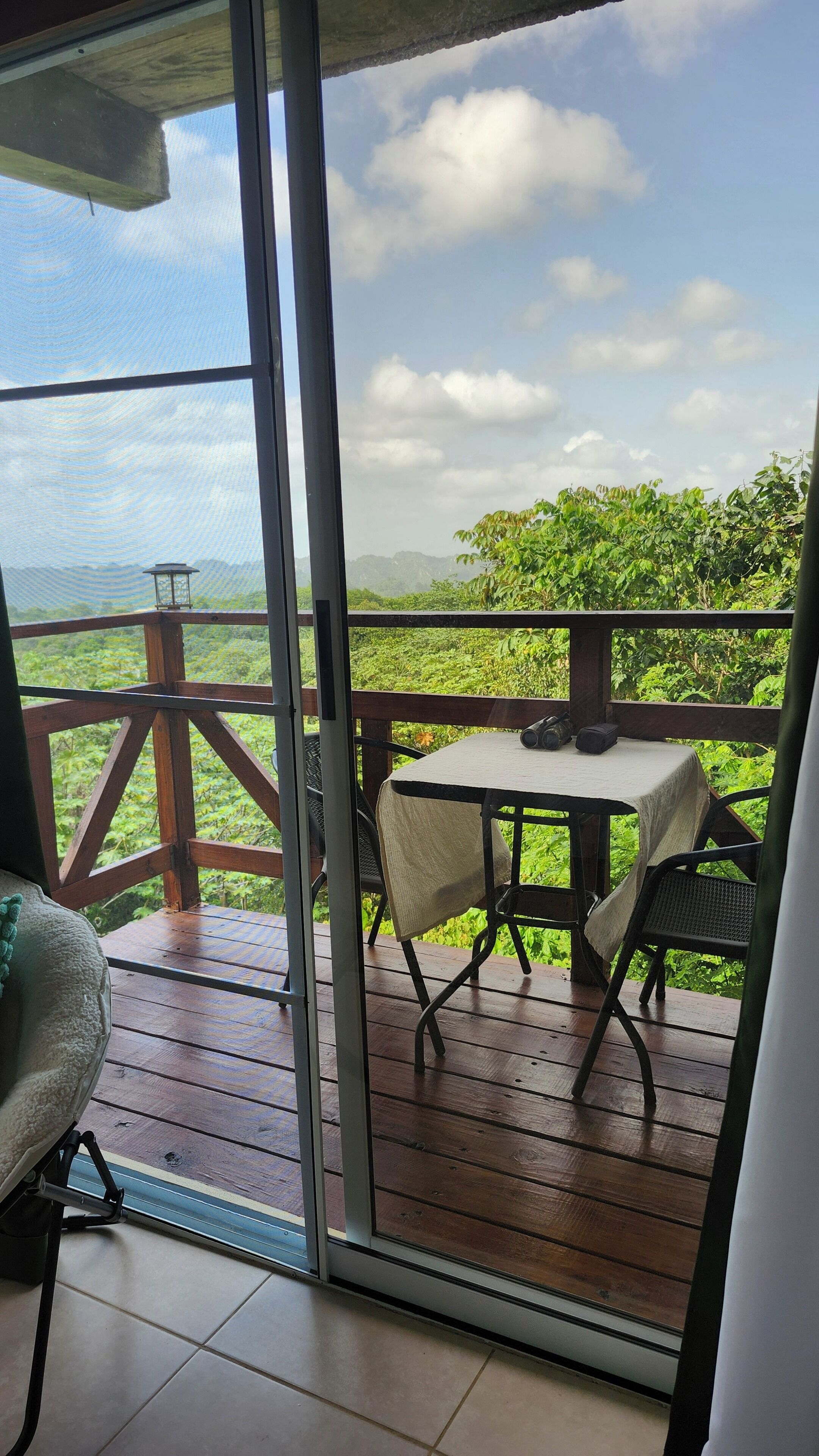 Un balcon avec une table et des chaises, une vue sur la verdure et un ciel dégagé.