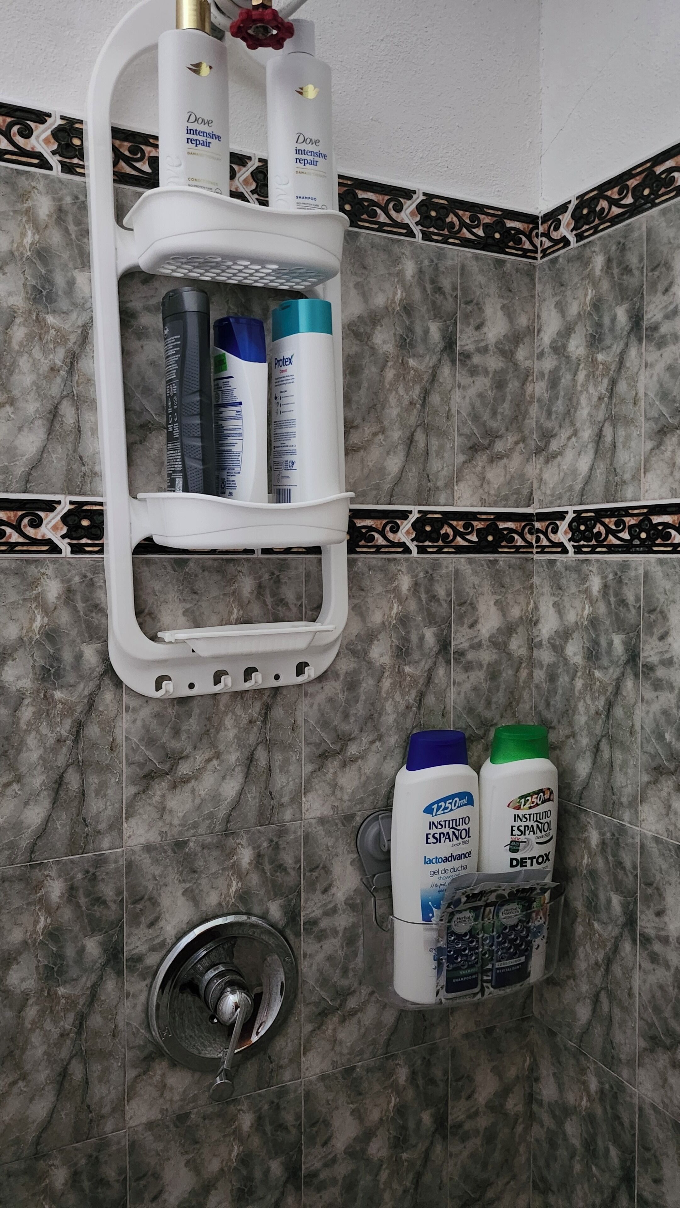 Un baño con pared de azulejos de mármol, un estante blanco que contiene champú y acondicionador Dove, y un cabezal de ducha.