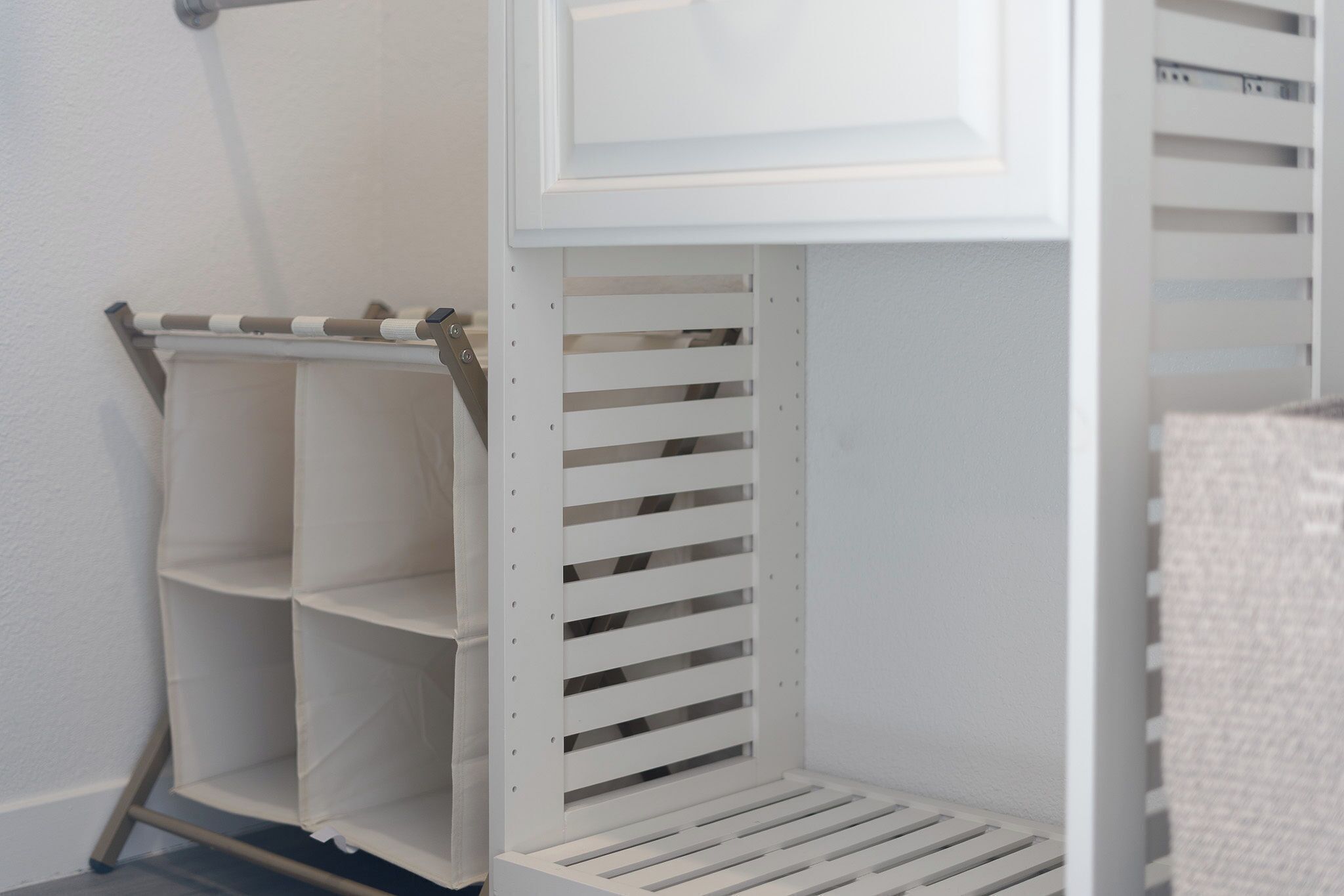 Een witte kast met open planken en een kledingroede.