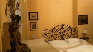 Ein Hotelzimmer mit einem Bett, einer Zimmerpflanze in einer Glaskuppel, zwei gerahmten Bildern an der Wand und einem Nachttisch mit einer Lampe.