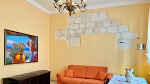 Ein Zimmer mit einer Couch, einem Tisch mit floraler Tischdecke, einer dekorativen Wand und einem Gemälde einer Küstenlandschaft.