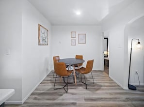 A dining area with a round table and four chairs, white walls, and a light floor. - Cozy Browne’s Addition Apt Near Downtown (Spokane)