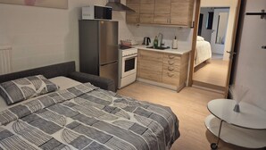 Ein kleines Schlafzimmer mit Bett, einer Kochnische und einem durchgehenden Türspalt erkennbaren Badezimmer.