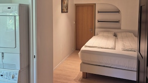 Ein Schlafzimmer mit einem Bett, Holzboden, einer Tür und einer Waschmaschine.