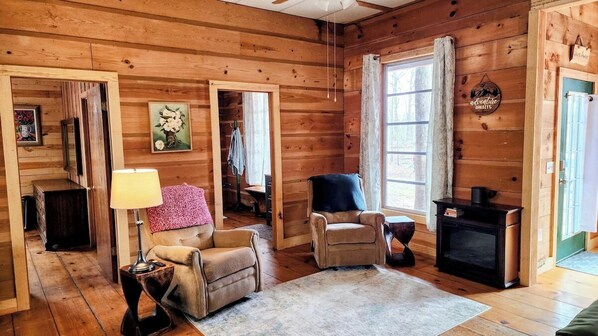 L’intérieur d’un chalet confortable, avec des murs en bois, une cheminée, un canapé et un fauteuil.