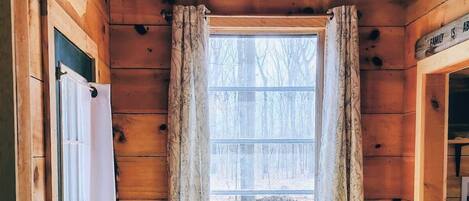 A wooden cabin interior with a window, a chandelier, and a door.