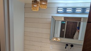 A bathroom with a white toilet, wooden cabinets, a sink with a black basin, and a mirror above the sink. - Beamsville Modern Rustic Suites (Lincoln)