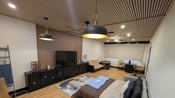 A modern living room with a sofa, a coffee table, a TV, and a wooden ceiling. - Beamsville Modern Rustic Suites (Lincoln)