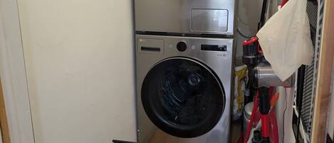 A compact laundry room with two stacked washing machines, a drying rack, and a vacuum cleaner.