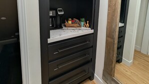 A kitchen with dark cabinets, a marble countertop, and a coffee maker. - Beamsville Modern Rustic Suites (Lincoln)