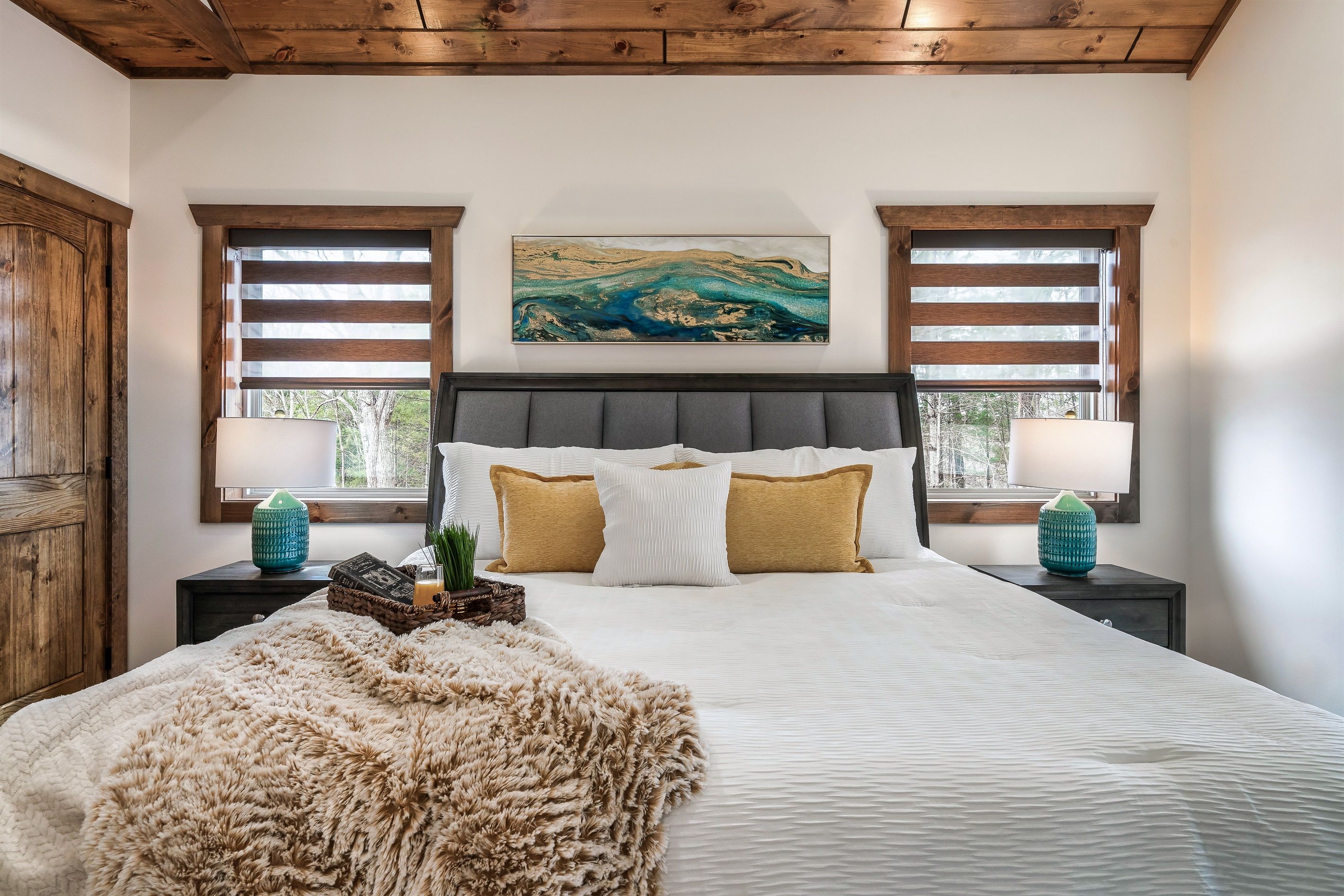 A bedroom with a large bed, wooden headboard, and two windows with blinds.