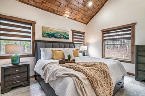 A bedroom with a large bed, wooden headboard, two bedside tables, and a view of the outdoors through windows. - Free Dollywood Tickets, Luxurious, Modern, A+Location, Fire Pit (Sevierville)