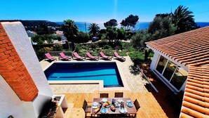 A pool with a view of the sea, a dining area with a table set, and a building with a tiled roof. - Casa da Madrugada - Peaceful haven with pool and ocean view in Salema (Salema)