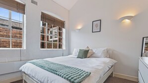 Una camera da letto con un letto, pareti bianche, una parete in mattoni e una finestra con persiane.