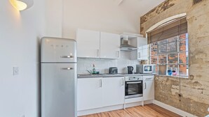Una cucina compatta con mobili bianchi, forno integrato, microonde e frigorifero.