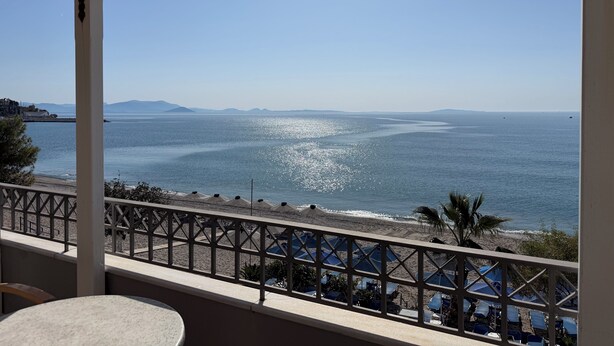 Un balcon avec vue sur la mer, une plage avec des parasols et un ciel dégagé.