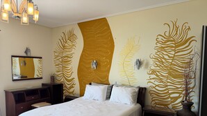 Une chambre d’hôtel avec un grand lit, une table de chevet, une commode, un miroir et un mur orné d’un motif de feuilles.