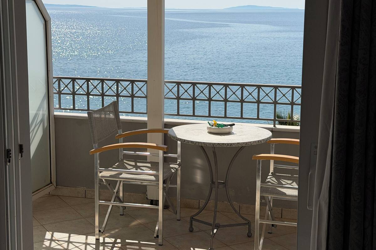 A balcony with a table and chairs, overlooking a body of water and distant land.