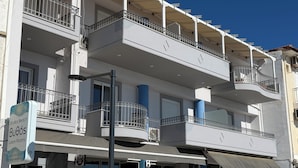Un immeuble à plusieurs étages doté de balcons, d’un espace extérieur aménagé pour s’asseoir et d’une enseigne indiquant « BuOos, chambres de luxe ».