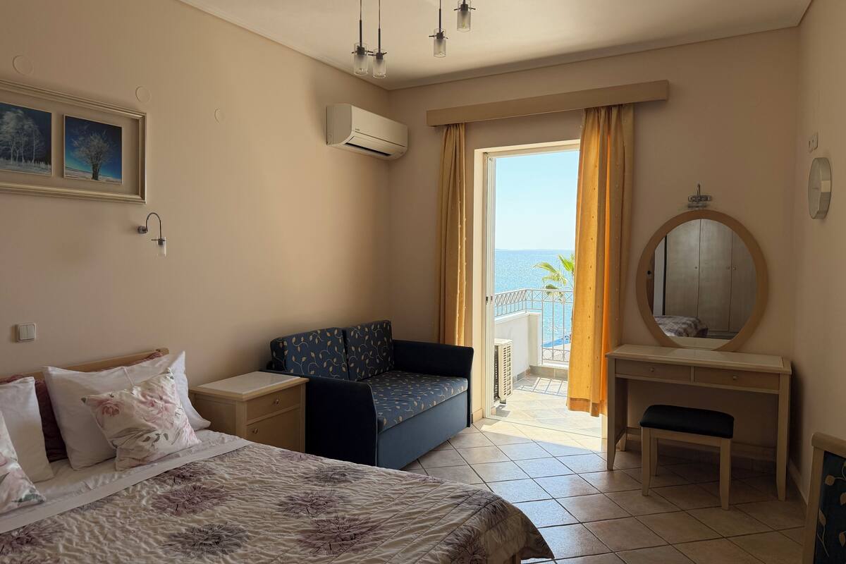 A hotel room with a bed, a sofa, a desk, a mirror, and a view of the sea.
