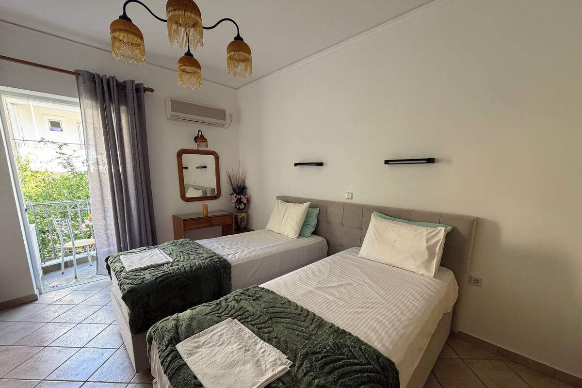 A hotel room with two beds, a balcony, a mirror, a small desk, and a hanging light fixture.